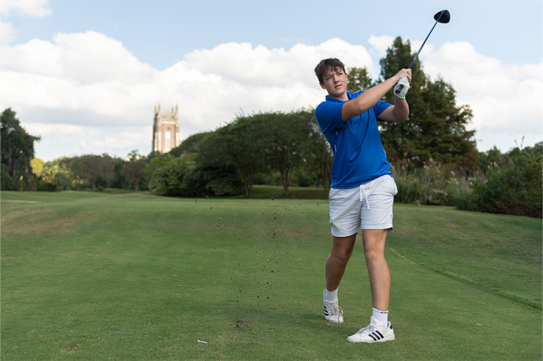 A participant at the 2025 Wolf Pack Athletics Golf Tournament takes a swing with Holy Name of Jesus in the background.